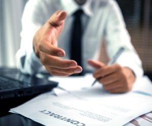 businessman extending his hand and a contract on table