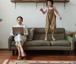 woman working with daughter jumping on couch