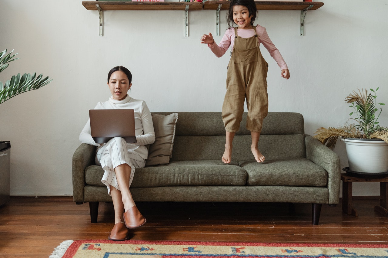 woman working with daughter jumping on couch