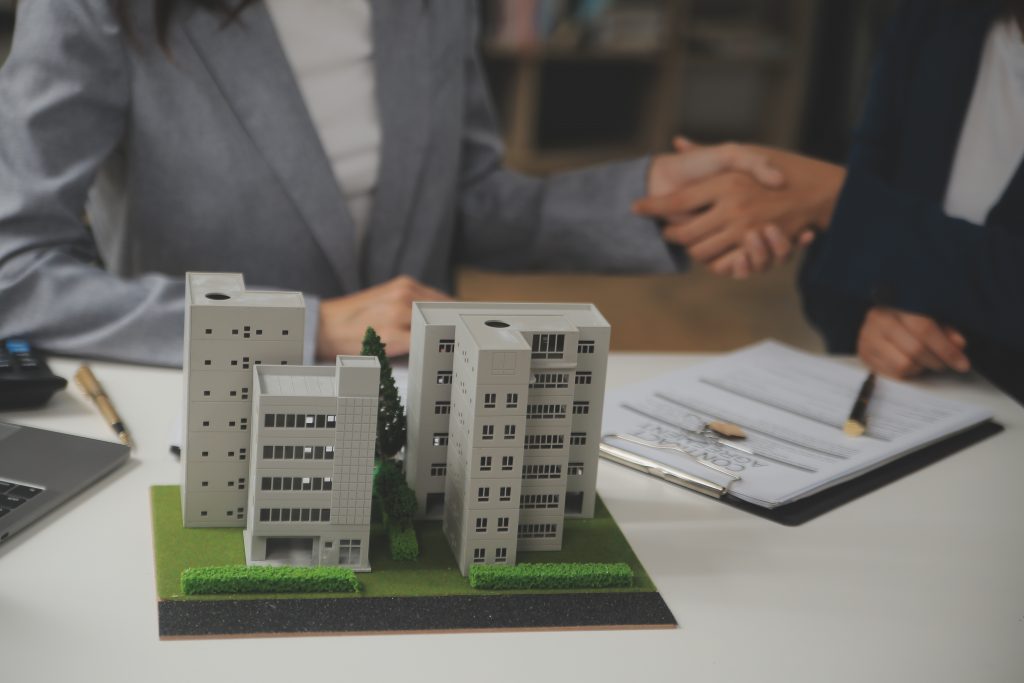 professionals shaking hands at a desk with a miniature model of a commercial building